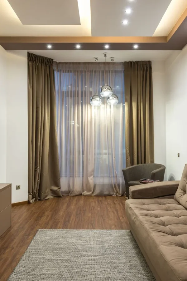 A sleek beige living room featuring a flat screen TV, sofa, and elegant lighting.
