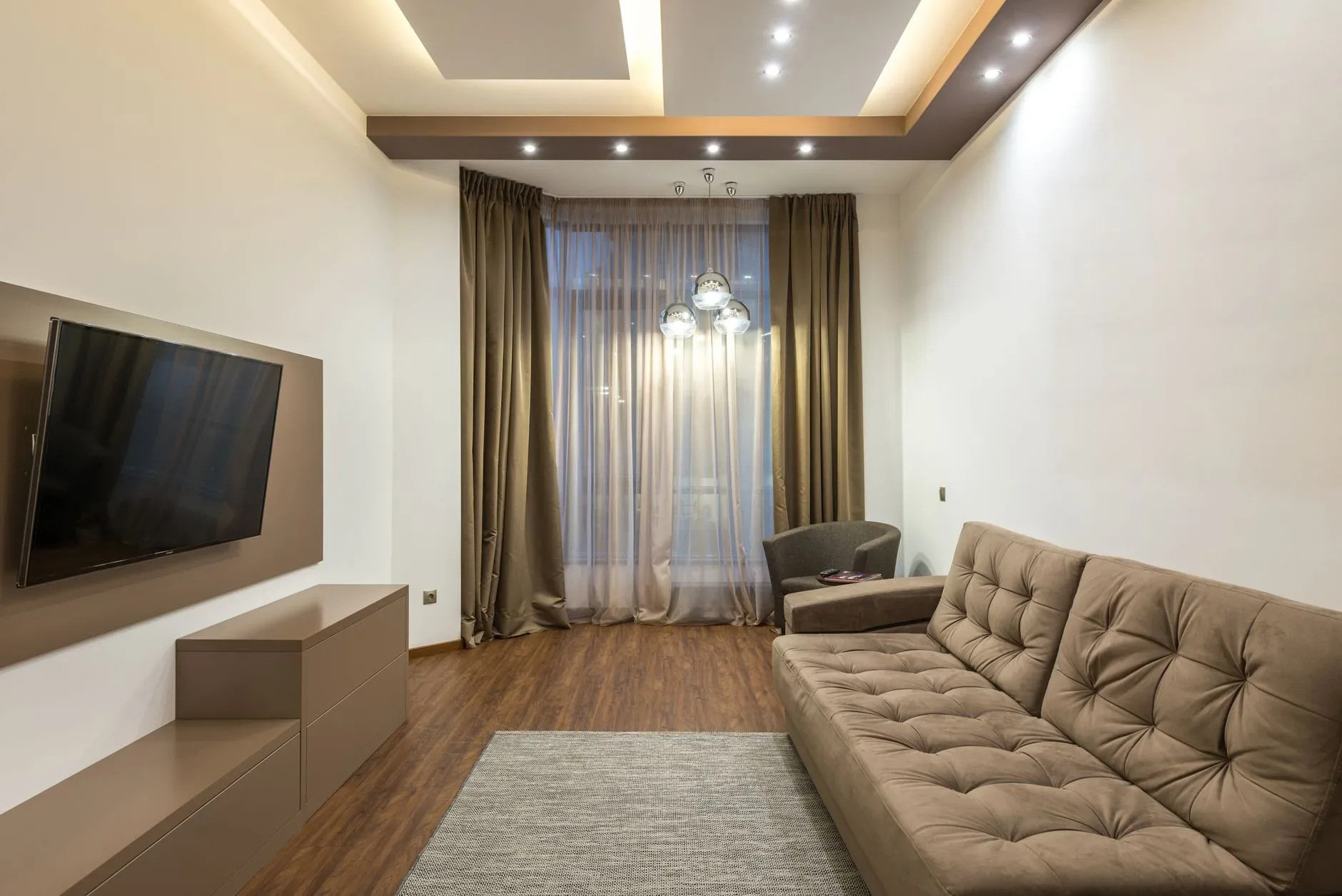 15 High-End Living Room Ideas for Small Spaces A sleek beige living room featuring a flat screen TV, sofa, and elegant lighting.