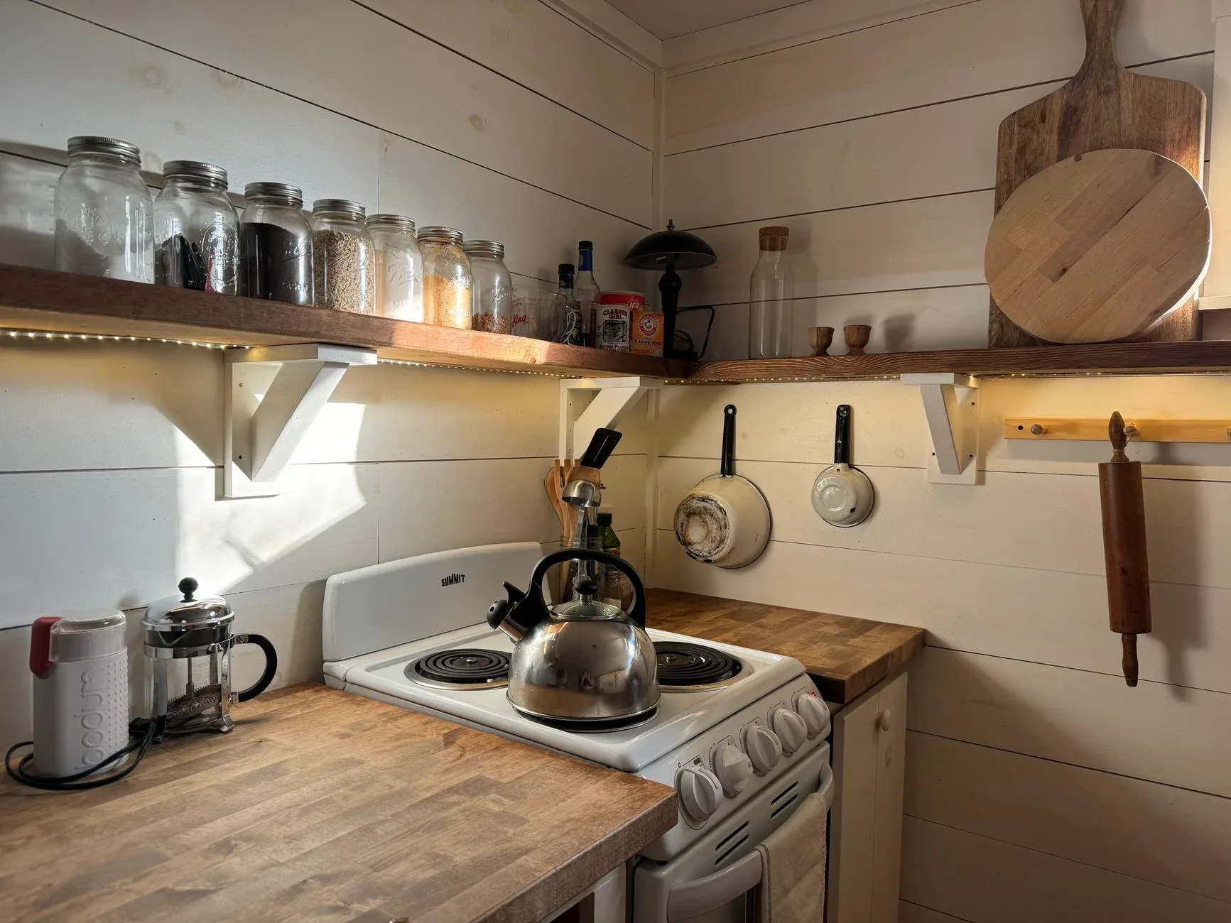 20 Cozy Kitchen Ideas That Make Cooking Feel Like the Best Part of Your Day A small rustic kitchen with a wooden shelf, stove, and cooking utensils, offering a warm and cozy atmosphere.