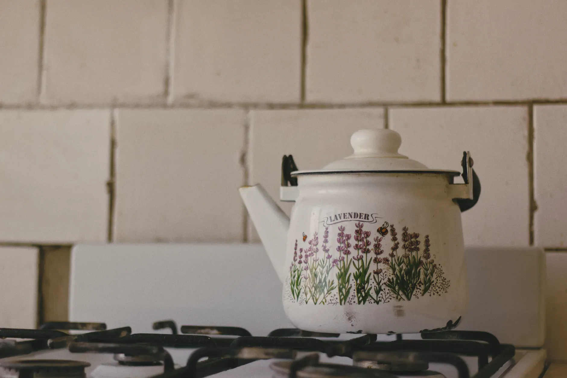18 Cozy Kitchen Decor Ideas for a Warm Home A vintage enamel teapot with lavender design placed on a kitchen stove, perfect for rustic decor themes.