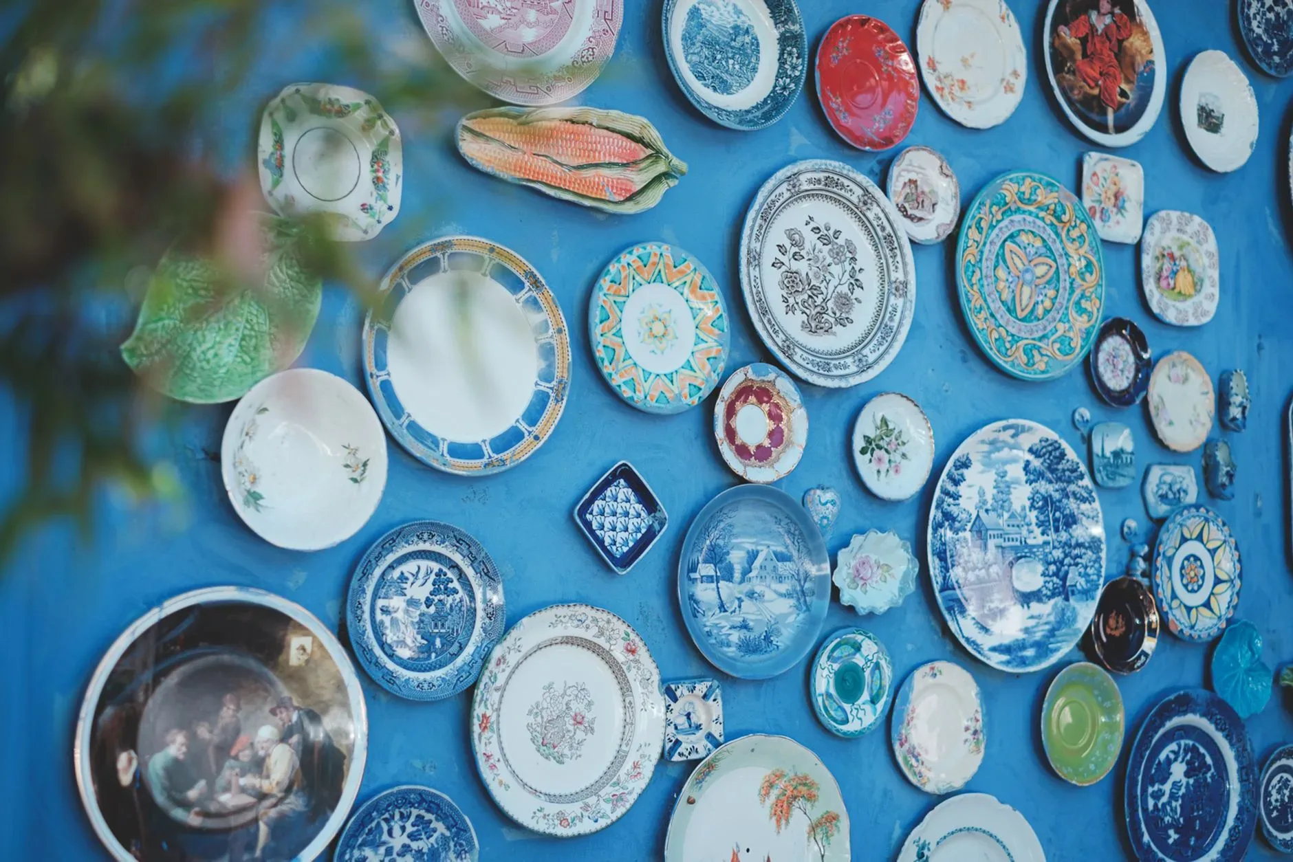 12 Wall Decor Ideas That Turn Every Blank Wall Into Something Beautiful Collection of various ceramic plates of different sizes and ornaments arranged on bright blue wall in studio