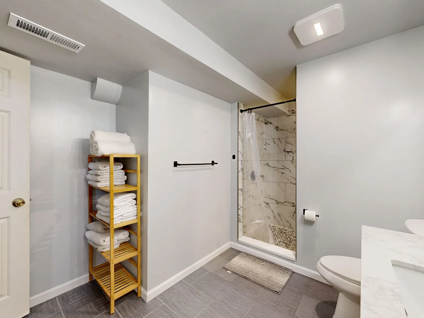15 White Bathroom Aesthetic Ideas on a Budget Contemporary bathroom featuring a marble-tiled shower and wooden towel rack.