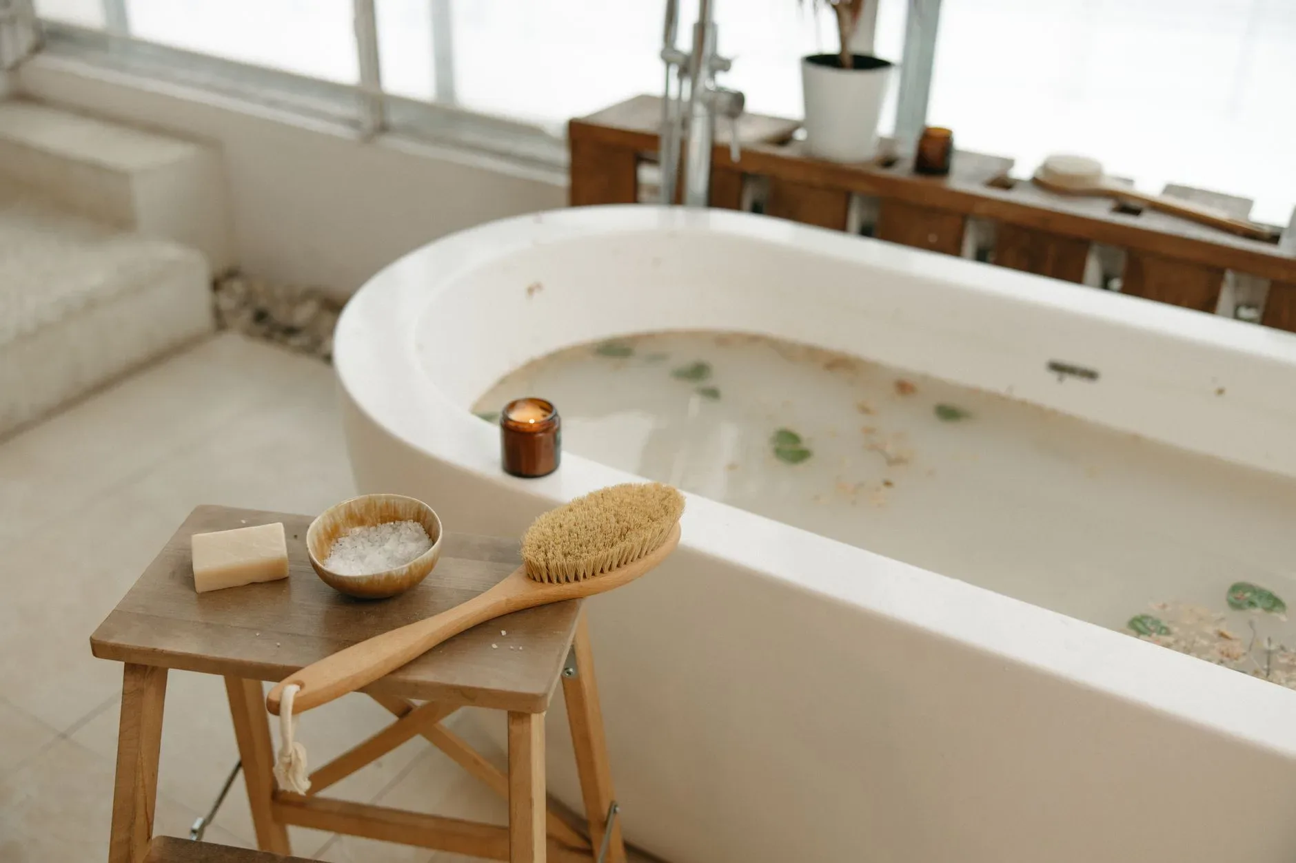 15 White Bathroom Aesthetic Ideas on a Budget Relaxing spa bath setup with luxurious essentials including soap, brush, salts, and candle.