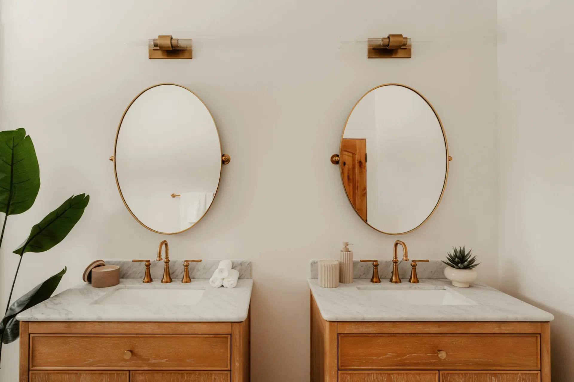 15 White Bathroom Aesthetic Ideas on a Budget Two wooden vanities with oval mirrors and gold fixtures.